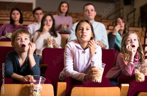 Numerous spectators eating popcorn and watching a movie at the cinema