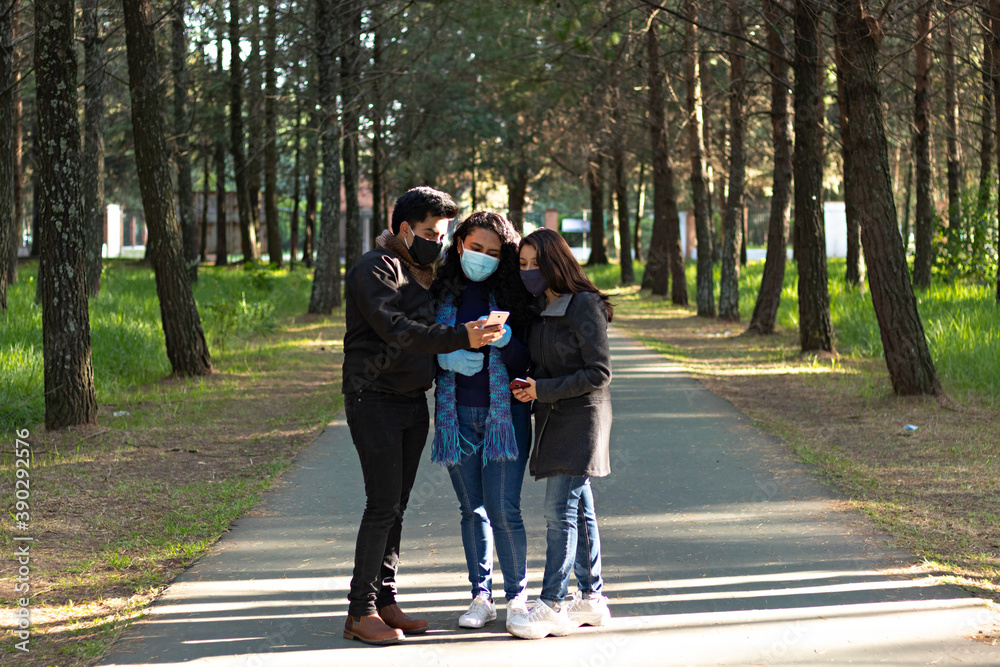group of friends, wearing mask, checking their cell phone while walking in a park