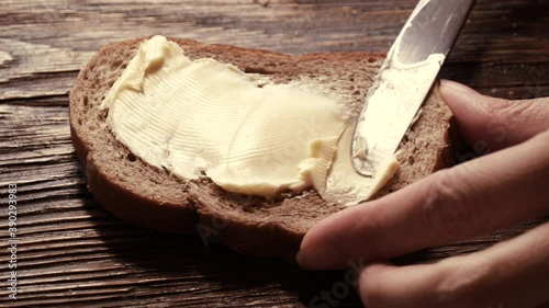 Close-up butter spreading on rustic rye bread with metal knife on wooden table photo