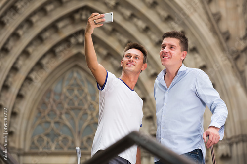 Two guys with luggage doing selfie at vacation.