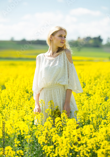 Young woman in yellow oilseed rape field posing in white dress outdoor
