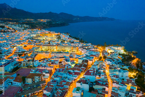 Illuminated evening view from drone of coastal Mediterranean city of Nerja, Andalusia, Spain