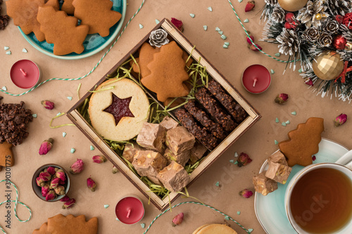 New Year and Christmas flat lay photo of box filled with homemade cakes on craft paper background, with decorations and baking around.