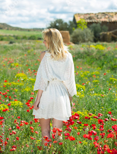 Back view of young woman in white dress walking and holding bouquet of poppies plants outdoor