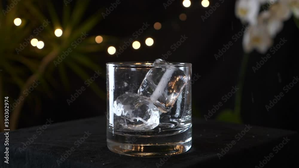 Two ice cubes fly into a fancy glass and a golden drink is poured into it, slow motion Two ice cubes fly into a fancy glass and a golden drink is poured into it, slow motion