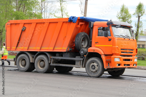 Road equipment on the street of the city in Russia. Russian truck 'Kamaz' dump truck orange with body and cabin, with three axles. Repair work on the road in the spring