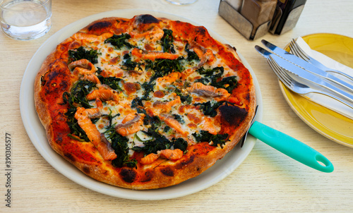Delicious cheese based fish pizza with fresh salmon pieces and green spinach