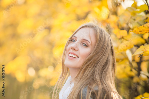 Portrait of a beautiful young woman against a background of colorful golden foliage in an autumn park. Attractive woman with light brown hair near bushes with yellow leaves. Fall season. Close-up.