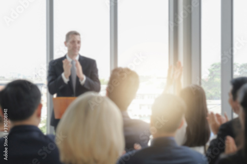 Blur photo background of happy business audience and speaker in corporate seminar event clapping hands together for celebration or congratulation, light effect.