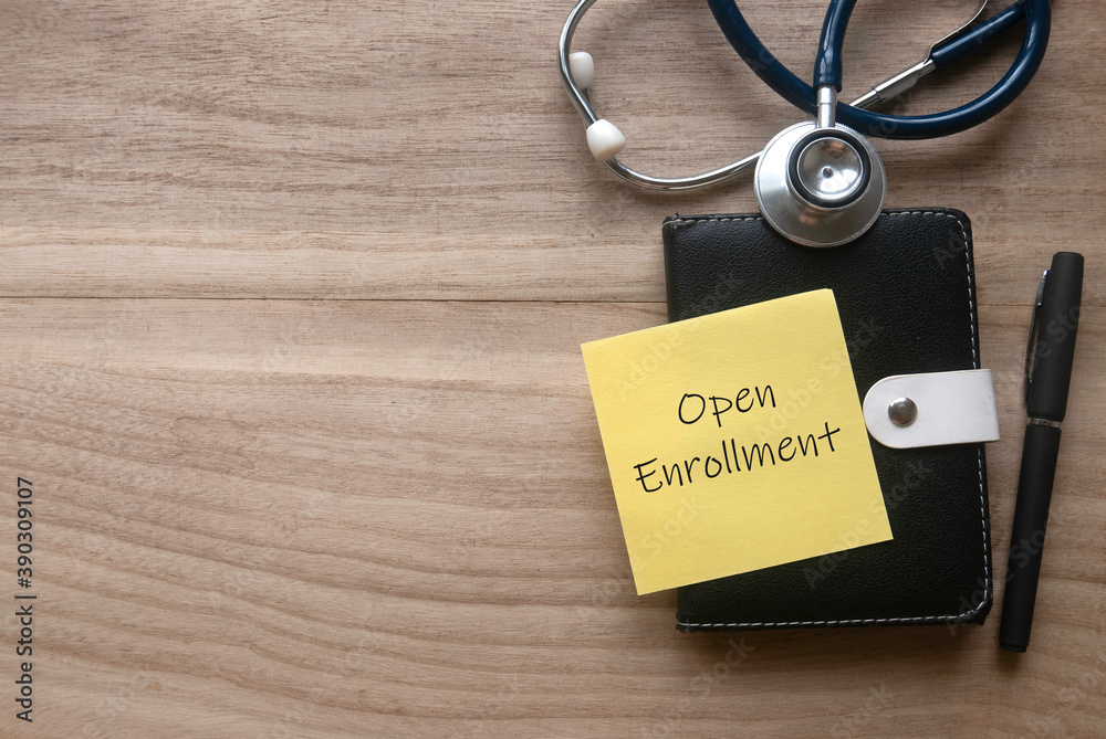 Top view of stethoscope, pen, notebook and yellow paper note written with Open Enrollment on wooden background with copy space. Top view of stethoscope, pen, notebook and yellow paper note written with Open Enrollment on wooden background with copy space.