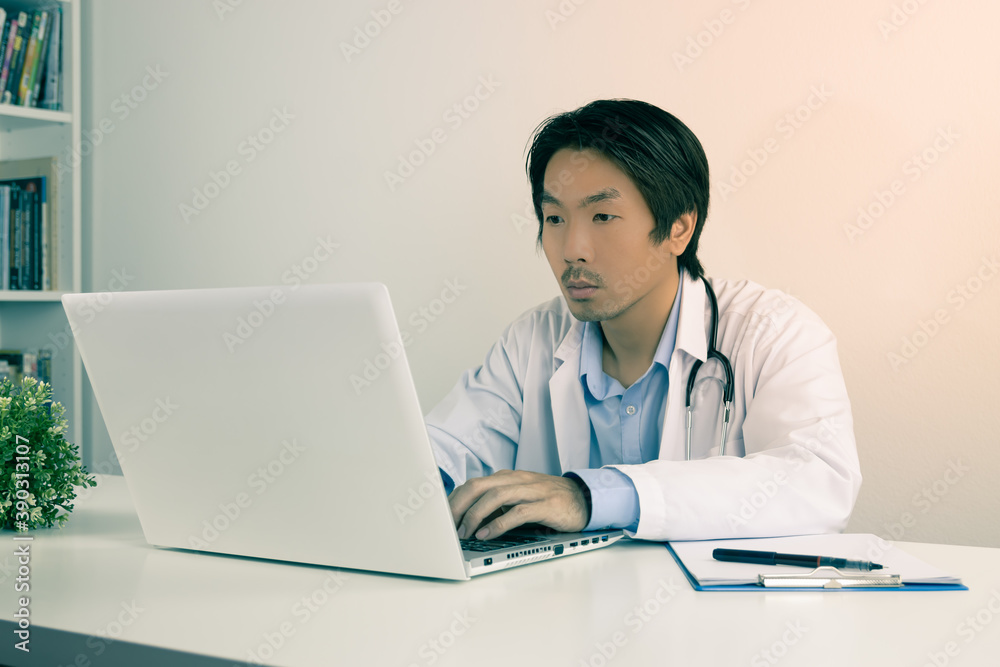 Young Asian Doctor Man in Lab Coat or Gown with Stethoscope Using Laptop Computer on Doctor Table in Office in Vintage Tone Young Asian Doctor Man in Lab Coat or Gown with Stethoscope Using Laptop Computer on Doctor Table in Office in Vintage Tone