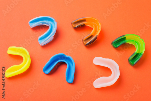 many boxing mouthguards of different colors, lies on an orange background photo