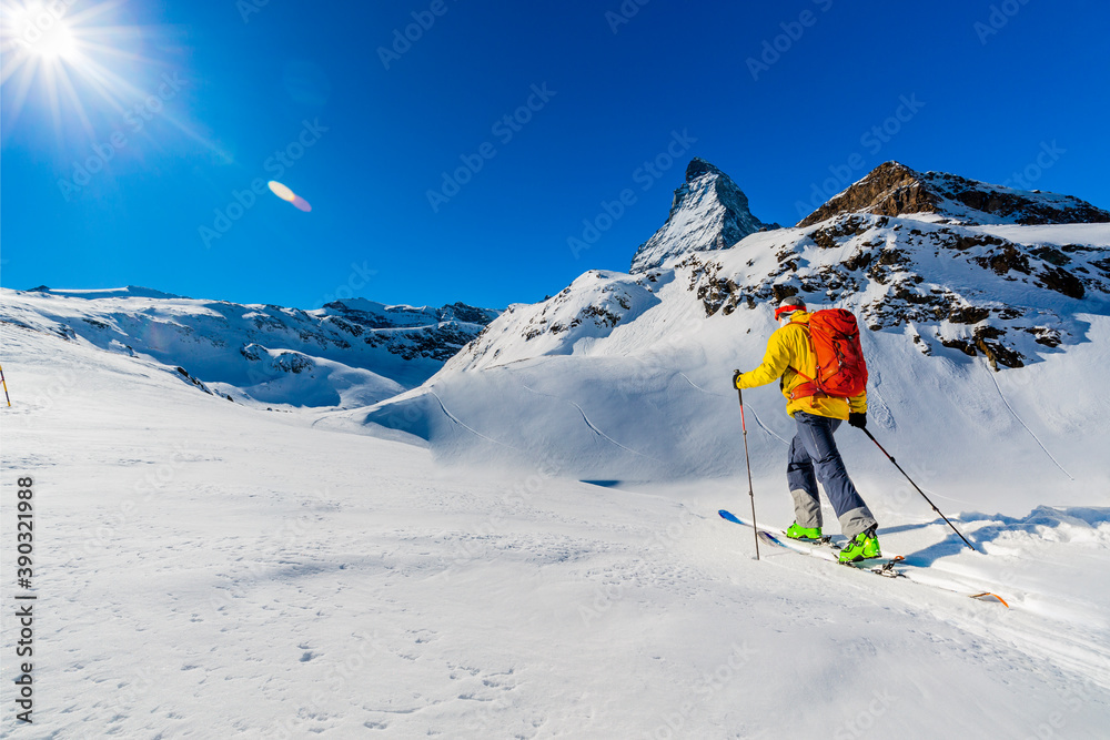 Man backcountry skiing on powder snow with Matterhorn in background, Zermatt in Swiss Alps.