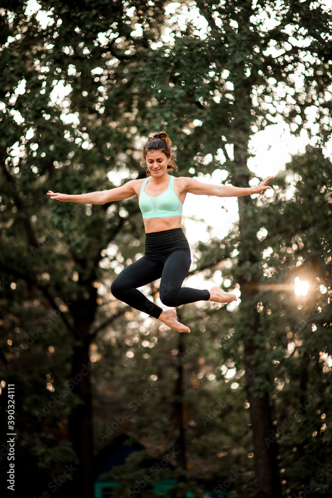 view of girl jumping up in the air against the backdrop of green trees