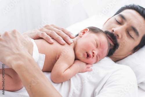 father with a baby girl at home sleeping. side view of a young man playing with his little baby in bed. a portrait of a young Asian father holding his adorable baby on white background.