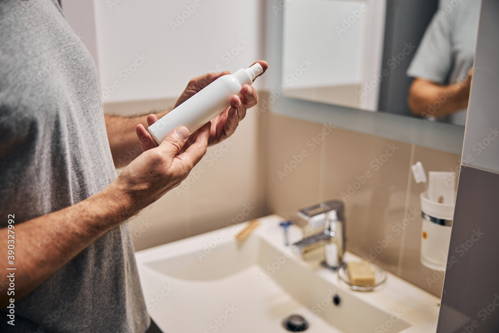 Gentleman in grey shirt with white cosmetic bottle in hands Gentleman in grey shirt with white cosmetic bottle in hands
