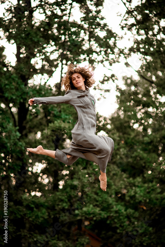 Young beautiful woman in long gray shirt magnificently jumps high in the air