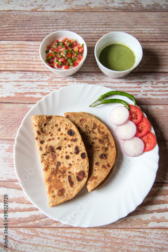 Alu Paratha along with vegetable salad in a plate along with condiments on a background