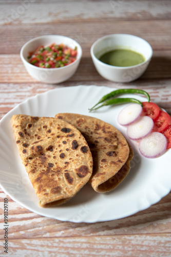 Close up of Alu Paratha along with vegetable salad in a plate along with condiments on a background