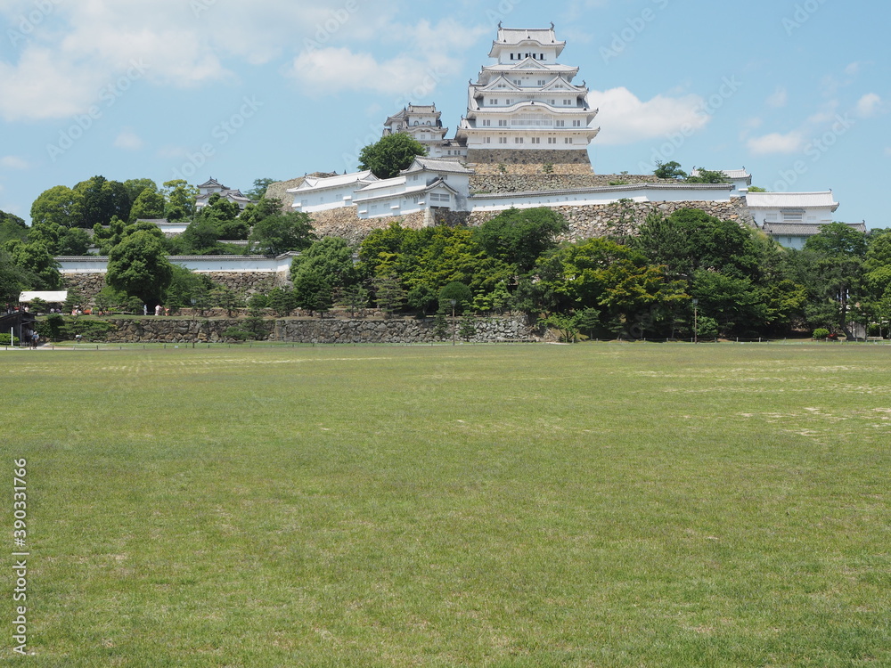 Ancient samurai castle in Himeji city in Japan with white walls, dark tile roofs and stone walls on a sunny day in summer with blue sky and white clouds