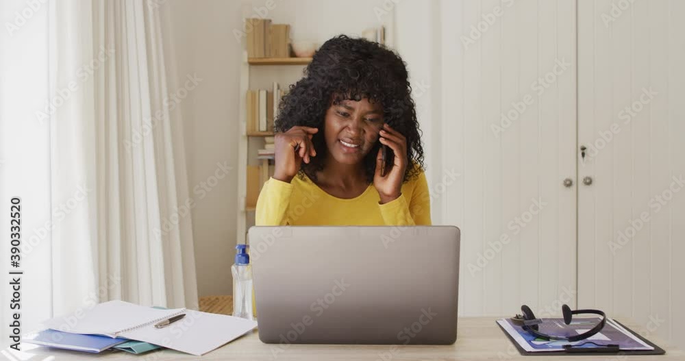 African american woman using laptop and talking on smartphone while sitting on her desk at home African american woman using laptop and talking on smartphone while sitting on her desk at home
