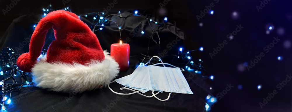 face masks put on next to a red santa claus hat and a candle in blur lights background - obrazy, fototapety, plakaty 