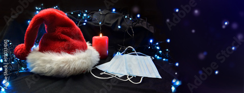 face masks put on next to a red santa claus hat and a candle in blur lights background