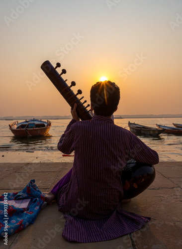 Fotografie a man playing sitar at bank of ganges river at varanasi and beautiful sunrise