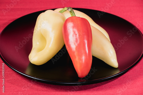 Red and yellow peppers on a black plate with a red background