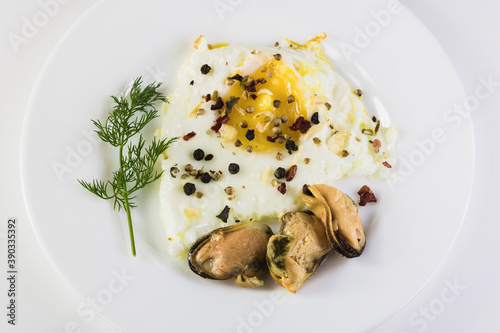 Mussels, fried egg, dill and spices on a white plate