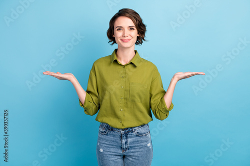 Photo of pretty cute lady short hairdo look camera hold two hands empty space demonstration showing wear denim jeans green shirt isolated blue color background