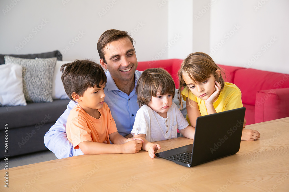 Cheerful dad and pensive kids watching movie via laptop together during weekend. Happy father sitting at table with children in living room. Fatherhood, childhood and digital technology concept Cheerful dad and pensive kids watching movie via laptop together during weekend. Happy father sitting at table with children in living room. Fatherhood, childhood and digital technology concept