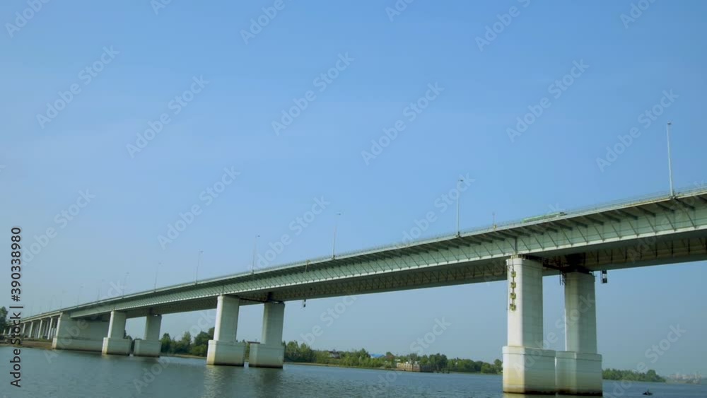 Automobile bridge over a wide river against the background of a blue sky. Traffic. The camera flies under the bridge. Automobile bridge over a wide river against the background of a blue sky. Traffic. The camera flies under the bridge.