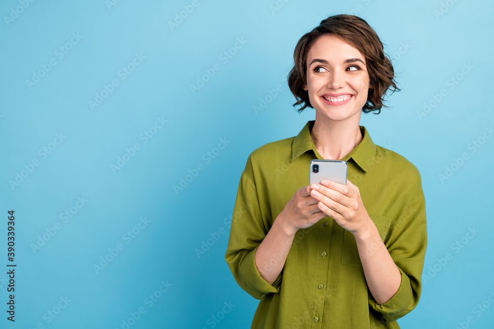 Photo of charming pretty lady short hairdo arms hold telephone playful look empty space grinning smile wear green shirt isolated blue color background Photo of charming pretty lady short hairdo arms hold telephone playful look empty space grinning smile wear green shirt isolated blue color background