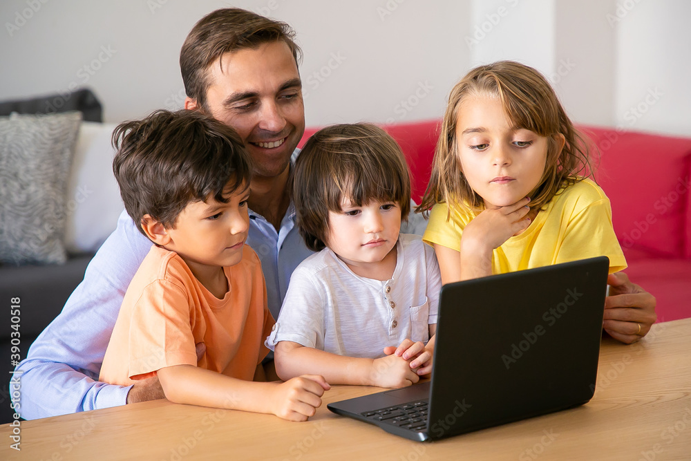 Happy dad and kids watching movie via laptop together. Caucasian father sitting at table and embracing cute children. Boys and girl looking at screen. Fatherhood and digital technology concept Happy dad and kids watching movie via laptop together. Caucasian father sitting at table and embracing cute children. Boys and girl looking at screen. Fatherhood and digital technology concept