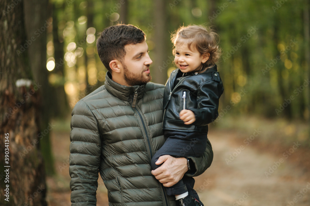 Portrait of beautiful little girl with her dad. Happy daughter on fathers hands in autumn forest. Two year girl