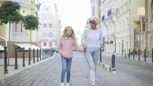 Wallpaper Mural Wide shot of relaxed happy grandmother and granddaughter holding hands and talking as strolling outdoors on sunny day. Portrait of Caucasian senior woman and little girl enjoying weekends in city. Torontodigital.ca