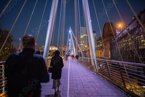 Pedestrians walking on a white bridge above the River Thames during nighttime