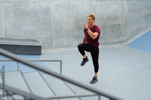 Young Man Running On Place Near Concrete Steps Outdoors. Handsome Caucasian Sportsman With Strong Muscular Body In Fashion Sportswear Warming Up Before Intense Workout.