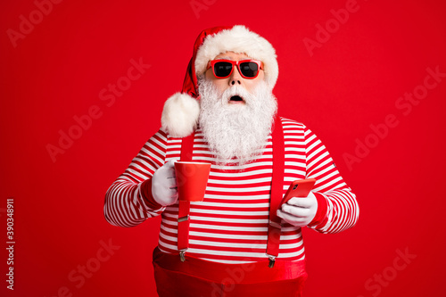 Portrait of his he nice handsome amazed stunned bearded fat overweight Santa drinking caffeine using device gadget 5g app browsing post smm isolated bright vivid shine vibrant red color background © deagreez
