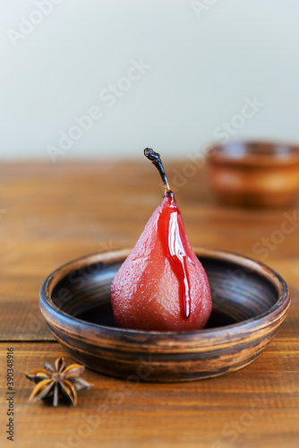 Poached pear in red wine with spices on a brown background.