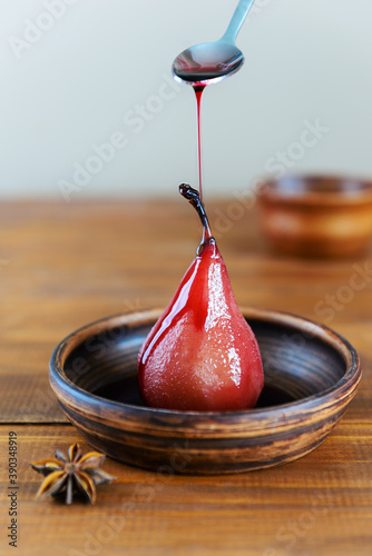 Poached pear with red wine syrup and spices on a brown background.