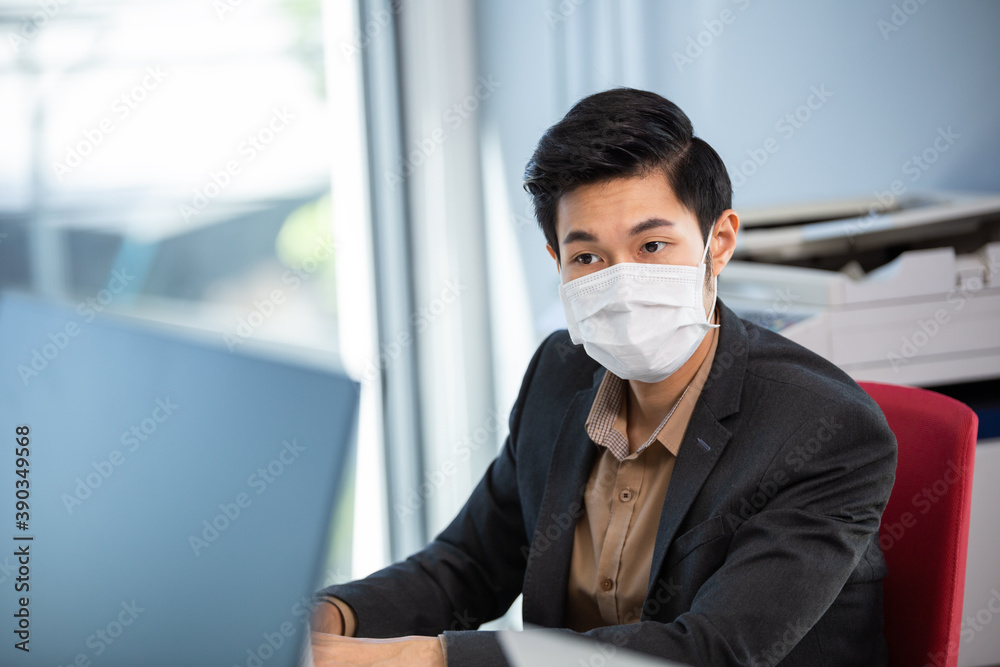 Portrait of employee man in face mask to prevent flu virus working with computer at office desk in reopen company. new normal people lifestyle with copy space