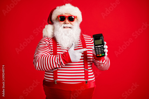 Portrait of his he nice handsome cheerful bearded fat Santa holding in hand demonstrating bank terminal wireless transaction isolated over bright vivid shine vibrant red color background © deagreez