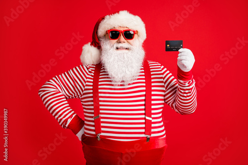 Portrait of his he nice handsome cheerful cheery Santa using holding in hand bank card bargain December shopaholic shopper isolated over bright vivid shine vibrant red color background © deagreez