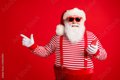 Portrait of his he nice handsome cheerful bearded fat overweight Santa using device app 5g showing copy space shopping gift present surprise isolated bright vivid shine vibrant red color background © deagreez