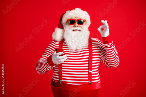 Portrait of his he nice handsome attractive cheerful glad bearded fat overweight Santa using device app 5g sale showing ok-sign isolated on bright vivid shine vibrant red color background © deagreez