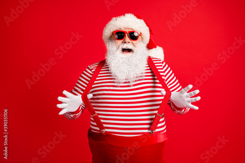 Portrait of his he nice handsome attractive comic childish cheerful cheery grey-haired Santa wearing gloves having fun pulling suspenders isolated over bright vivid shine vibrant red color background © deagreez