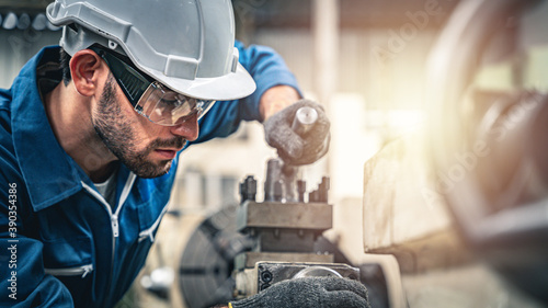Male engineer in blue jumpsuit and white hard hat operating lathe machine.	
 photo