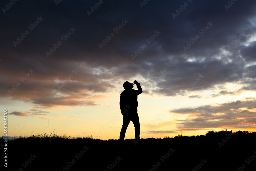 silhouette of a drinking man against the sunset